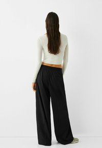 Valkoinen pitkähihaisen paita yhdistettynä löysiin mustiin housuihin. Asusteessa on sileä tekstuuri ja minimalistinen muotoilu, jossa on joustava vyötärö.