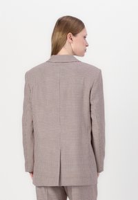 Rutete blazer i beige og brune farger, med skreddersydd passform, skjærende slag og enkelt vent bak. Materiale: teksturert stoff.