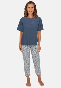 Navy blue t-shirt with white text, paired with white pants featuring a small floral pattern in blue and navy. Soft cotton fabric, relaxed fit.