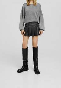 Černé kozačky do kolen s hladkým povrchem, masivními podrážkami, v kombinaci s šedým oversize sweatshirtem a skládací černou sukní.