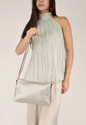 Bolso de mano tejido en plata con una textura suave, que cuenta con una correa desmontable. Presentado por una persona que lleva una blusa plisada en verde menta.