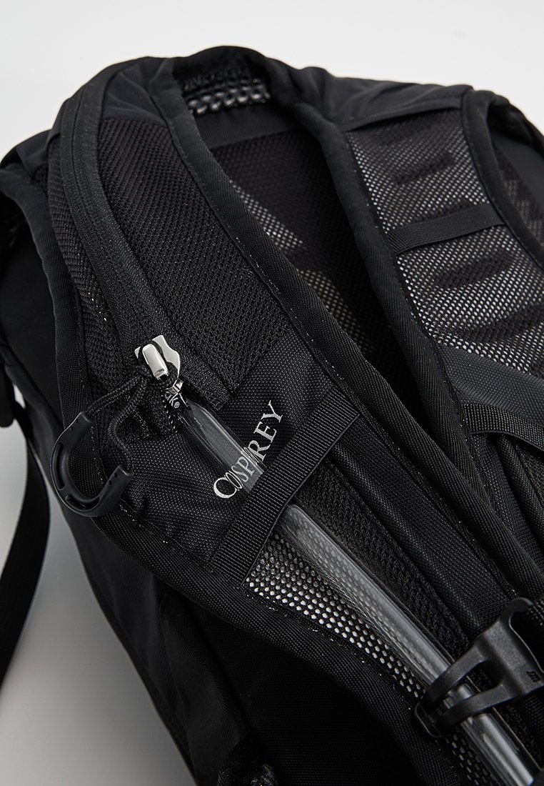 Mochila negra con paneles de malla, cremalleras y logotipo. Cuenta con correas ajustables y un diseño elegante para funcionalidad y comodidad.