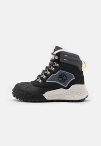 Botte mi-haute noire avec des accents gris, semelle blanche mouchetée, œillets en métal et col en fourrure. Présente un logo sur le côté et un profil de semelle texturé.