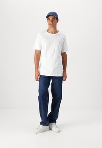 Hvit T-skjorte med korte ermer, blå caps, blå jeans, hvite joggesko, avslappet passform, minimalistisk design, har et lite logo på lommen på skjorten.