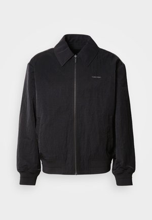 Mustast zip-up bomber-jaki, millel on tekstuuriga kangas, suur krae, elastsed mansetid ja vöökoht. Omab diskreetset logo detaili rinnal.