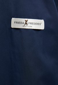 Marine stof met een gladde textuur, voorzien van een geweven label met de tekst "FRIEDA FREDDIES NEW YORK," aangekleed met een klein zilverkleurig logo.