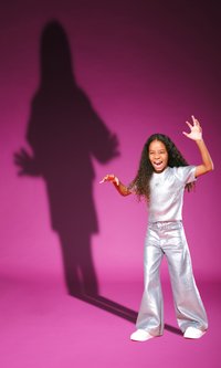 Silver, metallic top and pants with wide legs, set against a pink background. A shadow of the figure is cast on the backdrop.
