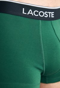 Groene katoenen boxershorts met een zwarte tailleband waarop "LACOSTE" in het wit is gedrukt. Glad materiaal met platte naden.