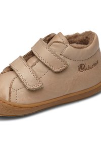 Scarpa in pelle beige con due cinturini in Velcro, soffice fodera interna, forma arrotondata e suola in gomma marrone chiaro. Presenta un logo sul lato.
