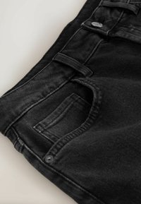Jean en denim noir plié, montrant la poche avant, la boucle de ceinture et le détail du bouton en métal sur un fond clair.