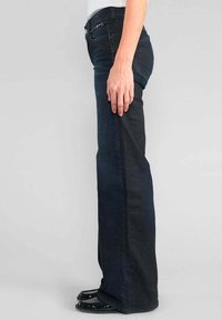 Jean en denim bleu foncé avec une coupe droite, présentant une taille mi-haute et des poches latérales. Le tissu a une texture lisse.