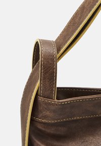 Sac en cuir marron à texture lisse, avec des coutures jaunes contrastantes et un design de poignée pliée.