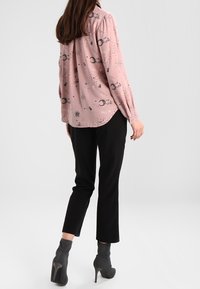 Ljusrosa skjorta med knappar och svart himmelprint, matchad med svarta slim-fit byxor och grå ankelstövlar med hög klack.