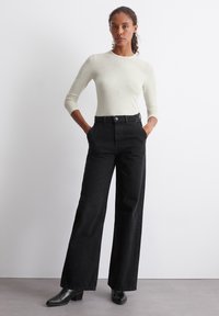 Langermet, lysegrå topp kombinert med høyt midje, vide svarte jeans. Outfiten har en jevn tekstur og subtile sømdetaljer.