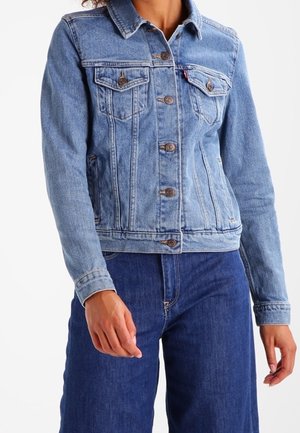 Person wearing light blue buttoned denim jacket with flap chest pockets and dark blue denim jeans.