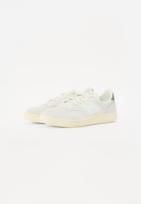Light grey suede sneakers with perforated detailing, white "N" logo, and soft green accents on the heel, featuring a beige rubber sole.