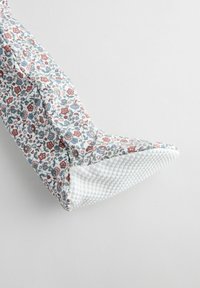 Kengät, joissa on kukkakuvioinen kangas, teräväkärkinen valkoinen kumipohja, jossa on tekstuuria. Hallitsevat värit ovat valkoinen, sininen ja punainen. Reunat on viimeistelty siististi.