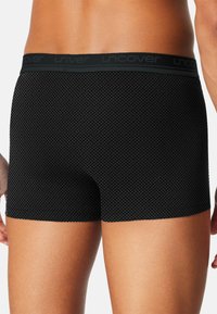 Schwarze Boxershorts mit einem strukturierten Diamantmuster, ergänzt durch einen glatten schwarzen Bund, der den Markennamen "uncover" trägt.