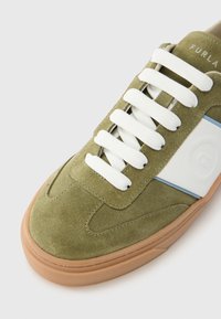 Zeleni tenis s antilopa s bijelim vezicama, s bijelim i plavim bočnim dijelom te smeđim gumenim potplatom. Glatka, teksturirana površina s detaljima.