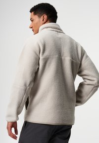 Fleecejacke in hellem Beige mit strukturierter Oberfläche, ausgestaltet mit hohem Kragen und seitlichen Taschen, entworfen für Komfort und Wärme.