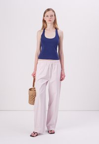 Marineblå tank top i lett stoff, kombinert med rosa og hvite stripete, løstsittende bukser. Modellen holder en vevd kurvveske og har på seg svarte sandaler.