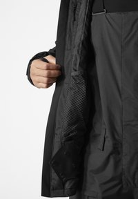 Veste noire avec une doublure intérieure texturée, une poche zippée et un poignet à bouton. Le design met l'accent sur la durabilité et la fonctionnalité.
