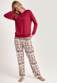 Red long-sleeve top with crew neck and ribbed hem, paired with cream-colored pants featuring a floral and geometric pattern in red and navy.