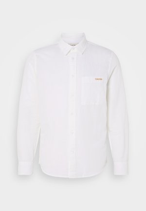 White long-sleeve shirt made of lightweight fabric, featuring a button-down collar, front pocket, and a small logo in the upper left corner.