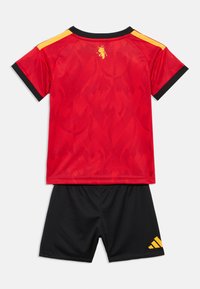 Κόκκινη ποδοσφαιρική εμφάνιση με κοντομάνικο πουκάμισο με σχέδιο φλόγας και μαύρες λεπτομέρειες, σε συνδυασμό με μαύρο σορτς και κίτρινο λογότυπο Adidas.