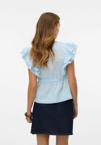 Blouse bleu clair avec des manches à volants, taille élastique et bordure en dentelle décorative, associée à une jupe en denim foncé. Tissu doux et coupe décontractée.