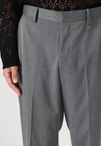 Grå skreddersydde bukser med et glatt, teksturert stoff. Har flat front, beltehemper og subtile legg, stylet med en svart strikket topp.