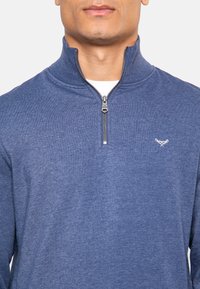 Jersey azul marino con cremallera y cuello alto, hecho de un tejido suave y texturizado. Presenta una cremallera metálica y un pequeño logo bordado en el pecho.