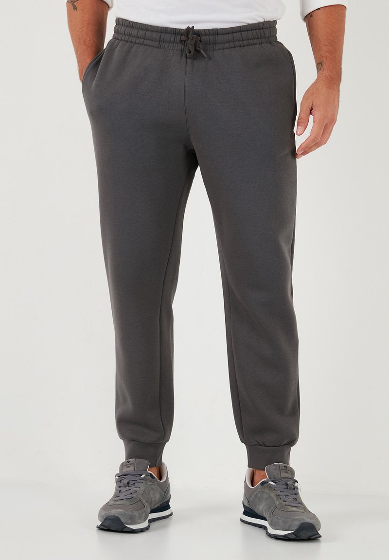 Grijze sweatpants met een taps toelopende pasvorm, elastische tailleband, trekkoord en zijzakken. Het materiaal lijkt zacht met een gladde textuur.