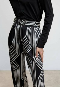 Black and white striped trousers with a smooth texture and wide legs. Features a matching belt with a rectangular buckle.