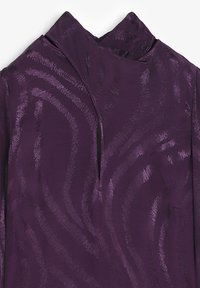 Tela morada con una textura suave, que presenta un patrón ondulado y un diseño de cuello alto, incluye una abertura frontal y un detalle de bolsillo.