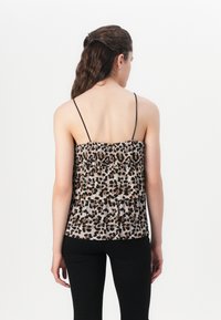 Majica bez rukava sa leopard uzorkom, sa nabranim dizajnom, koja ima tanke crne trakice i mekan, teksturiran materijal. Nosena preko crnih hlača.