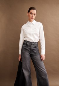 Camicia bianca con colletto classico, abbinata a jeans grigi scuri a vita alta e dalla vestibilità ampia. Tessuti lisci con un design semplice.