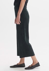 Dark green wide-leg pants in soft corduroy with a high waistband, paired with black flats. Smooth texture and clean lines throughout.