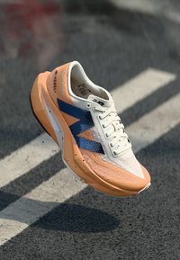 Pantof de alergare ușor cu partea superioară portocalie și gri, accente albastre, material tip plasă și talpă texturată. Prezintă un design distinctiv.