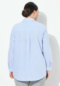 Camisa de rayas azul claro con cuello, mangas largas, detalle de pliegues en la parte posterior y puños abotonados. Tejido de mezcla de algodón con una textura suave.