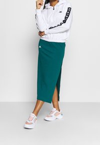 Valkoinen huppari mustilla sivuraitaeilla, yhdistetty teevihreään hameeseen, jossa on sivuhalkaisija. Yhdistetty valkoisiin ja vaaleanpunaisiin lenkkareihin.