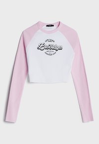 Avkortad långärmad topp med rosa ribbade ärmar och en vit ribbad kropp. Har en "Brooklyn"-grafik och text i svart på framsidan.