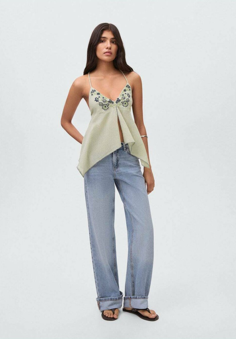 Light green sleeveless top with floral embroidery, asymmetrical hemline, paired with high-waisted, loose-fitting light blue jeans.