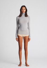 Svijetlosivi dugi rukav turtleneck top s prilijepim dizajnom, glatkom teksturom i uskom siluetom, u kombinaciji s bež kratkim hlačama.