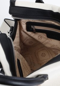 Czarna skórzana torebka z kremowym płótnem, zamykana na zamek. Wewnątrz znajduje się beżowa tkanina z powtarzającym się wzorem logo oraz licznymi kieszonkami.