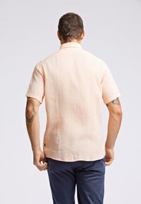 Korte mouwen, licht perzikkleurig linnen shirt met een relaxte pasvorm, knoopsluiting kraag en een klein merklabel aan de zijkant.