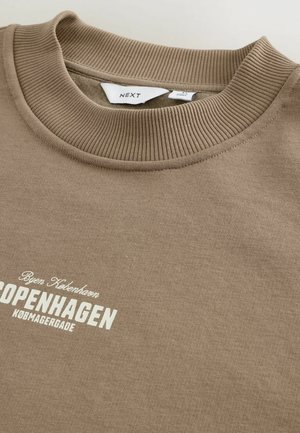 Sweat-shirt marron avec un col rond côtes et un tissu texturé. Présente un texte blanc portant l'inscription "COPENHAGUE" ainsi que d'autres détails de marque.