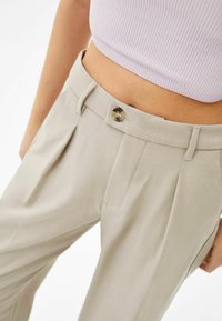 Beige op maat gemaakte broek met voorplooien, een gladde textuur en een ronde knoopsluiting bij de tailleband.