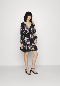 Vestido preto com estampa floral, mangas longas, apresentando padrões coloridos de flores, decote em V e barra franzida. Combinado com sandálias de salto pretas.