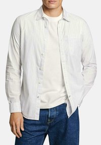 Randig skjorta i lätt tyg, med vertikala blå och vita ränder, en bröstficka och långa ärmar. Bar över en vit T-shirt.